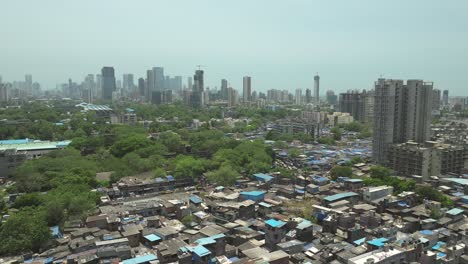 Drone-flyover-Dharavi-slum-rooftops-with-Mumbai-skyline-in-background,-India