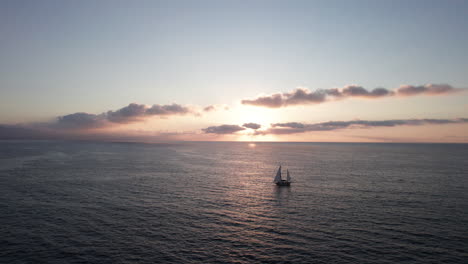 Sunset-Sailboat-Silhouette:-A-Serene-Ocean-Journey-with-Sunlit-Reflections-and-Gentle-Waves---Aerial-Drone-Footage