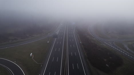 Tilt-up-aerial-flight-through-dense-clouds-above-German-freeway-with-driving-cars-in-autumn-season-on-cloudy-day
