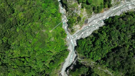 Aerial-straight-down-shot-of-floating-river-in-lush-jungle-and-small-suspension-bridge-during-sunny-day---Taiwan,Asia