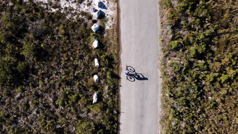 Top-down-aerial-over-MTB-cyclist-with-perfect-shadow,-road-through-fynbos
