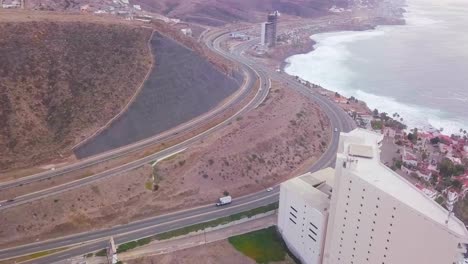 Blick-Von-Einer-Drohne,-Die-Um-Eine-Autobahn-Neben-Einem-Hotel-Nahe-Der-Küste-Und-Einem-Berg-In-Mexiko-Fliegt