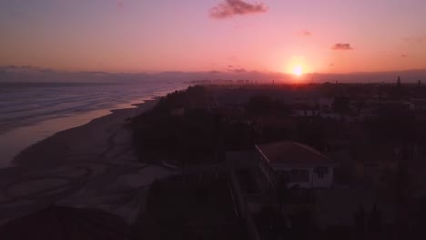 Drone-shot-of-pink-sky-sunset-over-the-ocean-beach-with-waves-in-Brazil