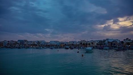 Marsaxlokk-township-waterfront-with-boats-during-sunset,-time-lapse-view