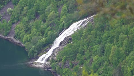 Bringefossen-Wasserfall,-Der-In-Den-Geiranger-Fjord-In-Norwegen-Fließt-–-Wasserfall-Durch-Telezoom-Objektiv-Gesehen-Mit-Verschwommenen-Ästen-Eines-Nahegelegenen-Baumes-In-Der-Oberen-Rechten-Ecke