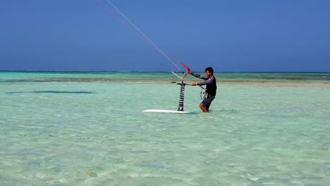 Adult-man-walks-in-shallow-sea-water-with-foil-kitesurfing-equipment-ready-to-action