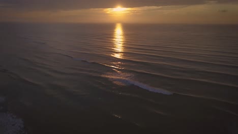Tilting-aerial-4k-shot-of-open-sea-in-sunrise,-big-waves-and-orange-sun-in-Brazil
