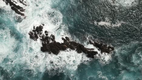Ocean-waves-splash-on-rocky-island-on-coast-of-Madeira-Portugal,-aerial-top-down