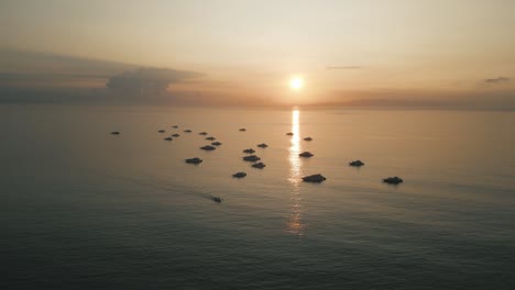 Bali-sunrise-aerial-shot,-boats-floating-in-the-ocean,-reflection-of-the-sun-in-the-calm-sea,-cinematic-atmosphere