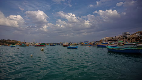 Barcos-Atracados-O-Anclados-En-La-Bonita-Bahía-De-Marsaxlokk,-Malta---Lapso-De-Tiempo-De-Nubes-De-Ensueño