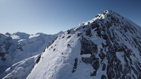 Cinematic-aerial-of-Mountain-Climber-on-steep-snowy-mountain-face-wall-in-winter---Blue-Sky-and-sunlight-in-backdrop---Orbiting-shot