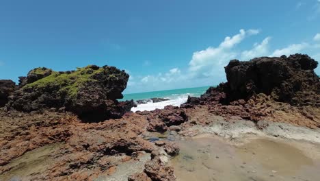 Tilt-up-handheld-action-camera-shot-of-small-waves-crashing-into-exposed-coral-rocks-during-low-tide-at-the-famous-tropical-Tambaba-beach-in-Conde,-Paraiba-Brazil-near-Joao-Pessoa-on-a-summer-day