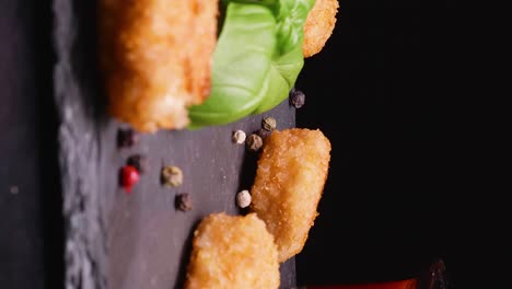 Vegan-chicken-nuggets-on-a-slate-plate-with-peppercorns-and-basil,-static-shot-against-a-black-background