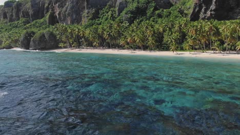 Tropical-Caribbean-sand-beach,-turquoise-blue-water,-rocky-cliff,-aerial-forward
