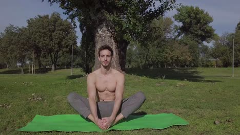 Slow-cinematic-shot-of-pretty-young-caucasian-man-doing-youga-stretch-pose-in-the-park