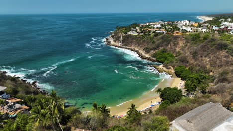 Aerial-view-away-from-the-Playa-Carrizalillo-beach-in-sunny-Puerto-Escondido,-Mexico---pull-back,-drone-shot