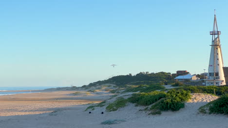 Glider-flying-by-Jeffrey's-Bay-Lighthouse-South-Africa-WSL-JBAY-Corona-Open-Supers-Boneyard-downtown-main-tourist-beach-late-afternoon-sunset-mid-summer-slow-motion-pan-to-the-left