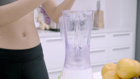Woman-in-sportswear-preparing-an-energizing-fruit-juice-after-exercise-with-a-blender-in-the-kitchen