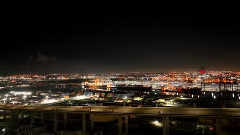 Highway-and-Long-Beach-Port-shipping-yard-at-nighttime---sliding-aerial-flyover
