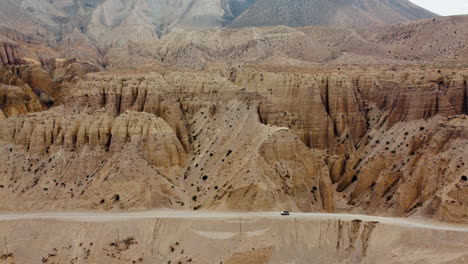 A-Scorpio-jeep-cruises-through-the-rugged-mountain-desert-of-Mustang,-Nepal,-with-breathtaking-natural-structures-and-landscapes-in-the-background