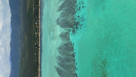 Vertical-aerial-flying-above-crystal-waters-towards-Domaine-de-Deva-,-New-Caledonia
