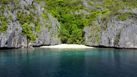 Aerial,-a-piece-of-Paradise-naturally-isolated,-Crystal-clear-water-and-white-sand-Beach-hidden-between-lush-Karst-rocks-and-tropical-Jungle,-El-Nido
