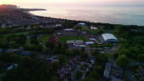 Colwyn-Bay-beautiful-summer-sunset,-Aerial-drone-pan-anti-clockwise-rotate,-focus-on-Eirias-Stadium---June-23