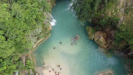 Bird's-eye-view,-Canyoneering-tourists-arriving-Kawasan-Falls-swimming-in-emerald-blue-water,-Cebu