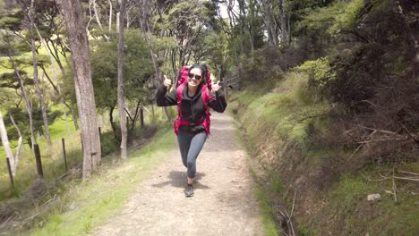 Asian-female-tourist-hiking-over-bush-and-forest-with-big-backpack,-thumbs-up-gesture