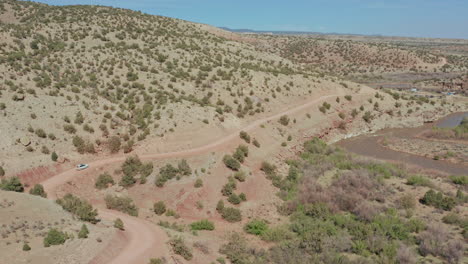 Car-drives-on-dirt-road-on-hillside-overlooking-remote-desert-river-valley