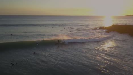 aerial-view-of-surfer-rides-the-ocean-waves-on-longboard-with-speed,-attacking-the-lip-of-the-wave-and-generating-an-impressive-amount-of-spray-with-huge-sunset-on-background