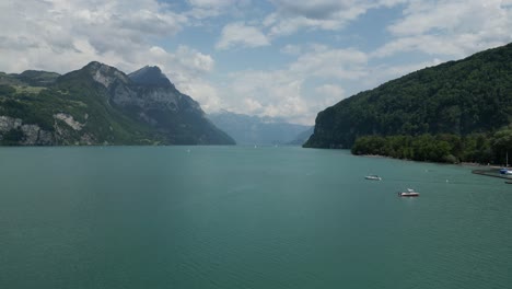 Boats-sailing-on-the-lake-in-front-of-a-small-village-in-Gäsi-Betlis,-Walensee-Glarus,-Weesen-Walenstadt,-Switzerland--drone-shot