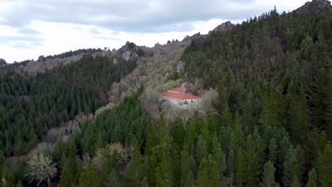 Spanish-monastery-hidden-among-tall-green-pine-trees-on-cloudy-day,-wide-aerial