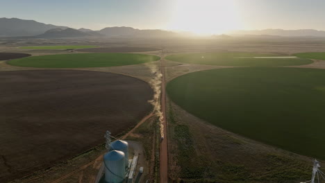Drone-shot-of-car-driving-on-dirt-road-in-near-pivots-with-green-farm-growth-in-Willcox,-Arizona,-wide-aerial-shot