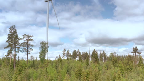 Tall-wind-turbine-in-woods-rotates-against-cloudy-sky