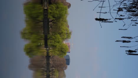 Vertical-Shot-Of-Public-Park-With-Lake,-Trees-And-Seagulls