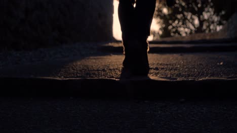 Legs-Of-A-Young-Man-Who-Is-Walking-Towards-The-Sunset-On-A-Cobblestone-Street-In-Slowmotion-in-france-with-summer-vibes-and-a-camera-in-the-hand-near-a-church