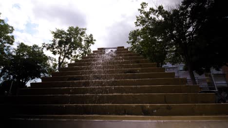 From-the-top-of-the-stairs,-a-fountain-cascades-down,-gracefully-pouring-on-the-sides-of-the-trees