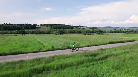 Seguimiento-Aéreo-De-Una-Joven-En-Bicicleta-Por-Una-Carretera-Rural-En-Un-Paisaje-Verde,-Rumania