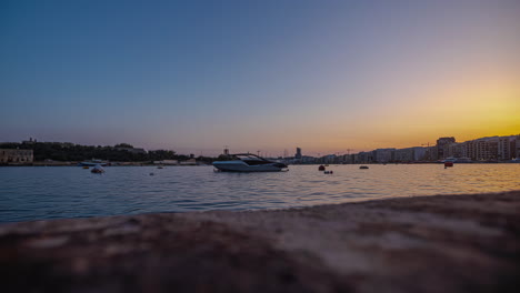 Boat-anchored-in-the-bay-at-sunset-offshore-from-Sliema,-Malta---time-lapse