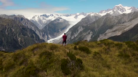 Young-traveler-enjoying-a-beautiful-scenic-view-of-Fox-Glacier-and-New-Zealand-mountains-after-hiking-to-the-top---aerial-pull-back