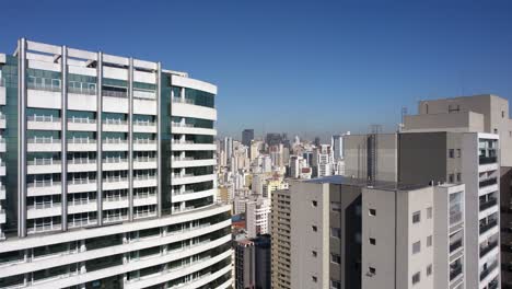 Drone-shot-rising-over-buildings,-revealing-the-concrete-jungle-of-sunny-Sao-Paulo,-Brazil