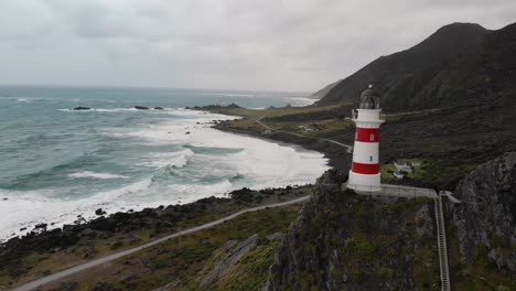 Fly-over-Cape-Palliser-lighthouse,-reveal-of-untouched-wildness-of-North-Island,-New-Zealand