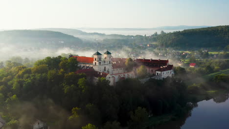 Aerial-drone-view-of-Benedictine-Abbey-over-Vistula-river-in-Tyniec-in-the-morning-fog,-Krakow,-Poland