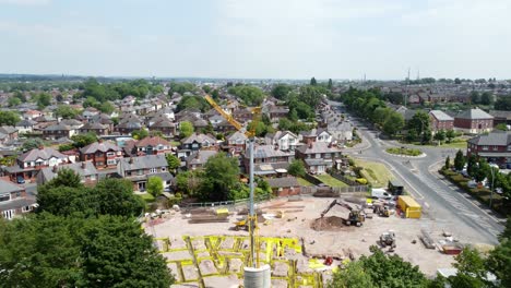 Tall-crane-setting-building-foundation-in-British-town-neighbourhood-aerial-forward-view-towards-suburban-townhouse-rooftops