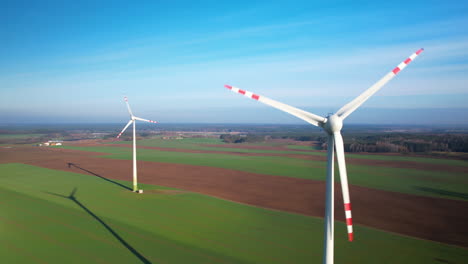 Aerial-View-Of-Pair-Of-Wind-Turbines-With-Spinning-Propellers-In-Green-Field