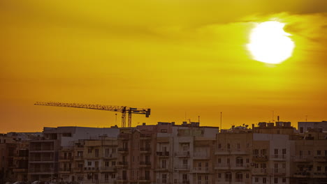 Bright-sun-setting-down-behind-rooftops-of-Maltese-township,-time-lapse-view