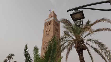 Looking-up-at-Koutoubia-mosque-tower-behind-Moroccan-lamp-and-palm-trees