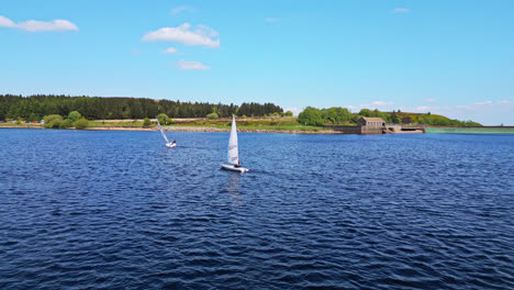 Amidst-the-picturesque-beauty-of-Winscar-reservoir-in-Yorkshire,-sailing-club-members-embark-on-a-thrilling-boat-race,-their-white-sails-standing-out-against-the-serene-blue-lake