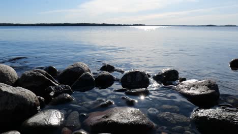 Calm-lake-scenery-with-rocks-on-coast-and-water-waving-smoothly